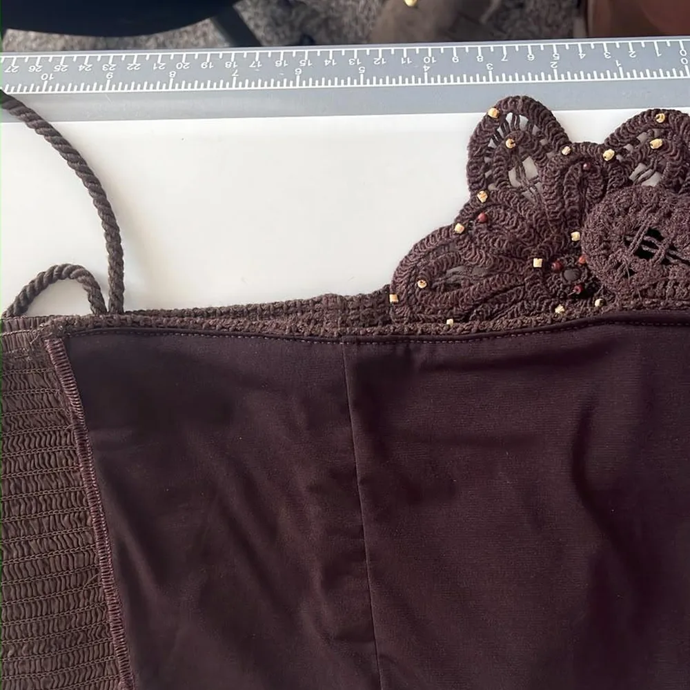 A brown top trimmed with crochet lace and gold beads, laid flat on the cutting table